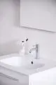 Waschtisch mit weißem Becken und Chrom-Wasserhahn von Ideal Standard. Im Hintergrund ein Spiegel und kontemporäre Badutensilien, darunter eine Zahnbürste und Zahnpasta.